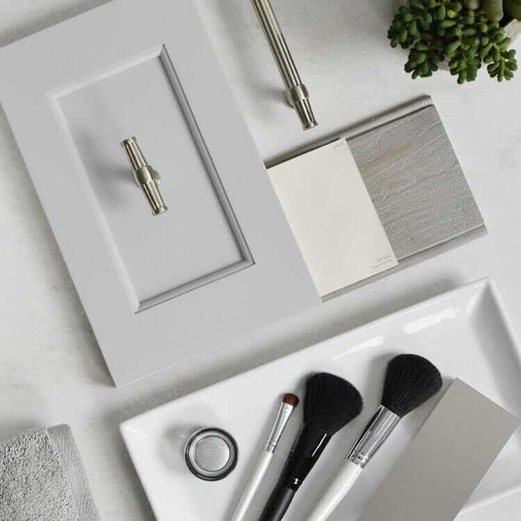 A soft gray inspiration board for a master bathroom remodel with flat laid samples of cabinet doors, finishes, hardware, etc. on a light gray countertop.