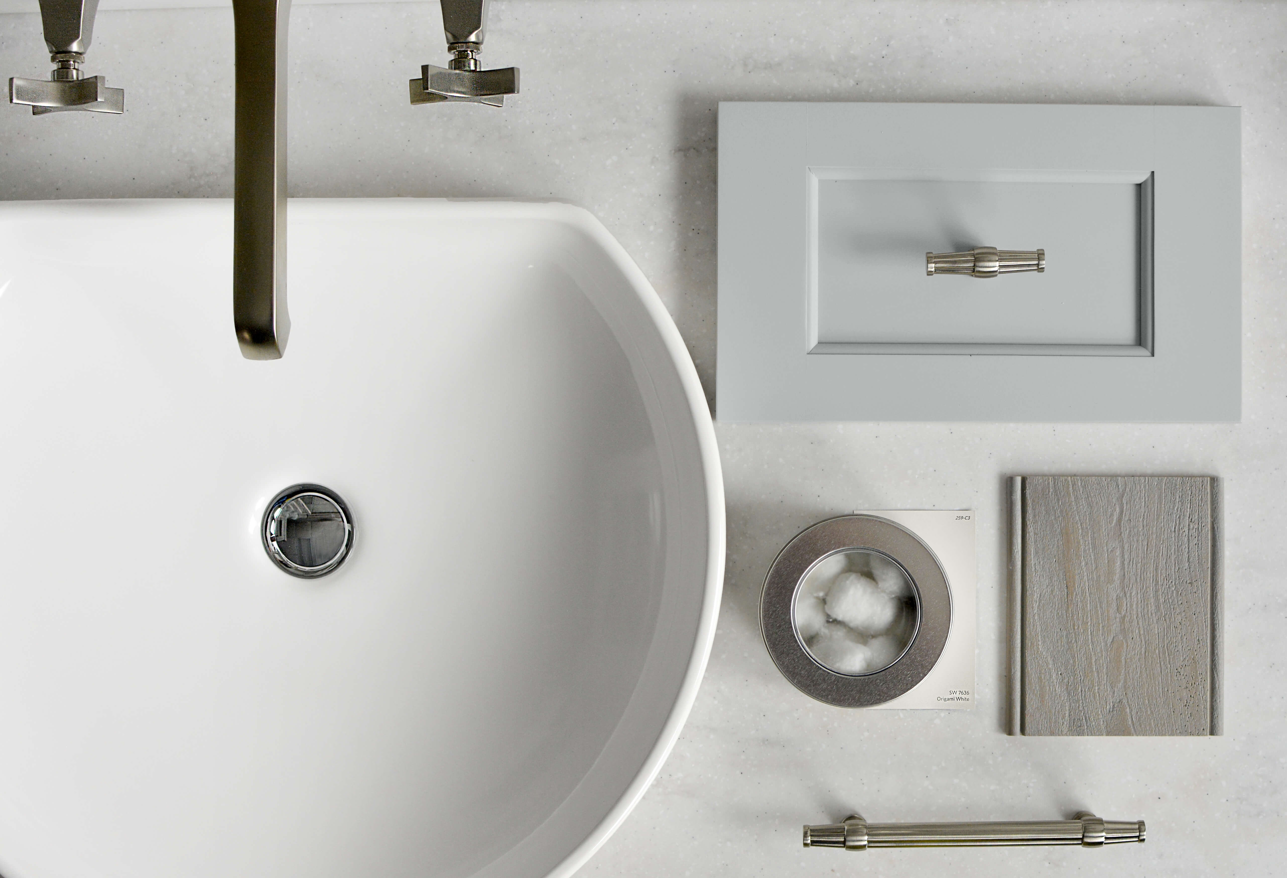 A soft gray inspiration board for a master bathroom remodel with flat laid samples of cabinet doors, finishes, hardware, etc. on a light gray countertop.