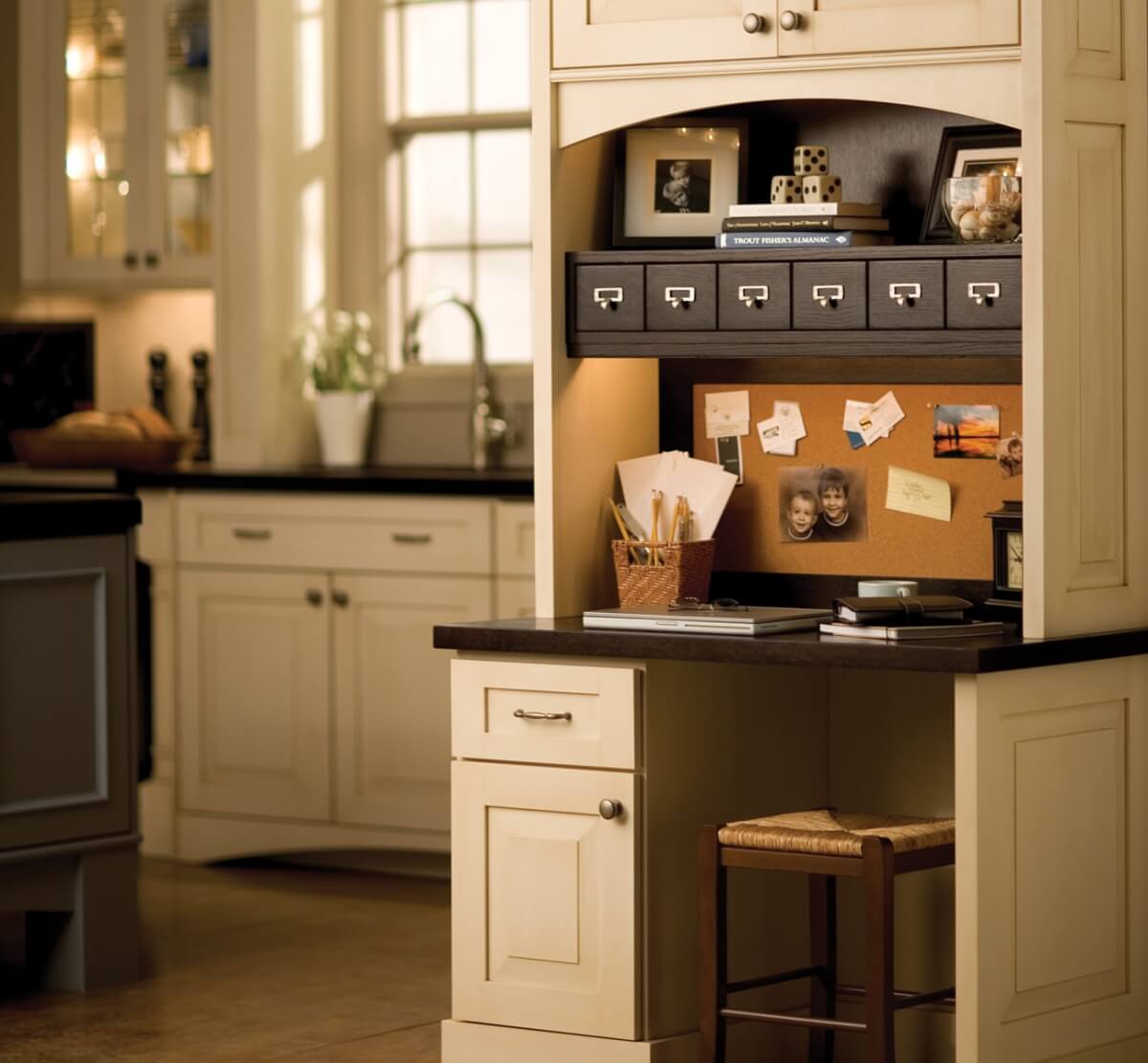 A small home office desk in the kitchen with apothecary drawers.