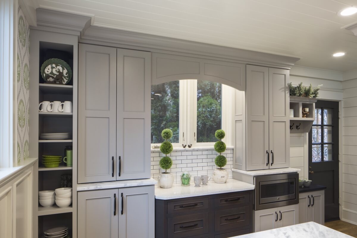 Gray painted and stained cabinets around a kitchen window.