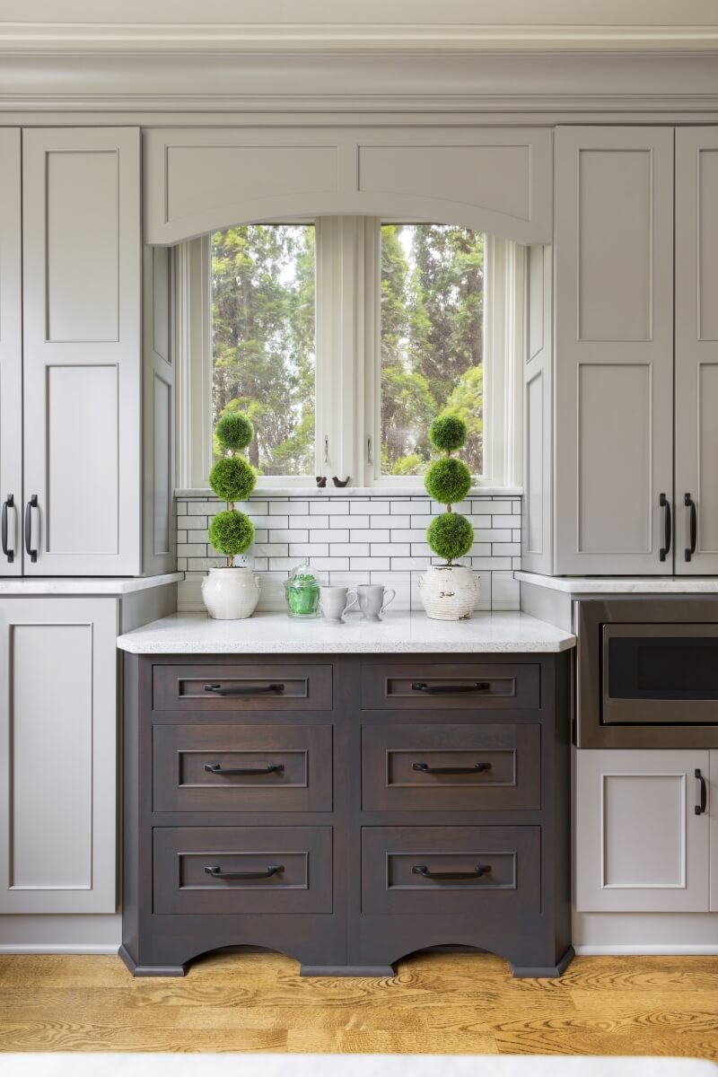 A base cabinet bump out with contrasting gray stain and gray painted cabinets that highlight the kitchen window space.