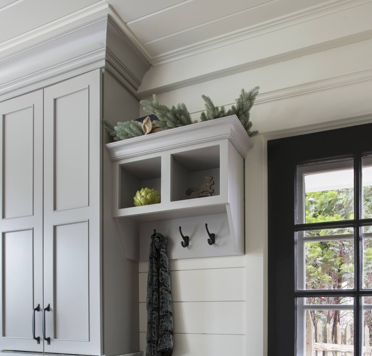 A light gray entryway cabinet with coat hooks at the entry way of the kitchen with white shiplap walls.