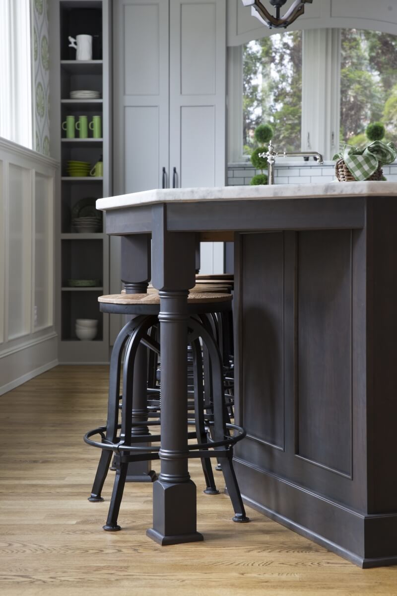 A close up of a gray stained kitchen island and turned post with stool seating.