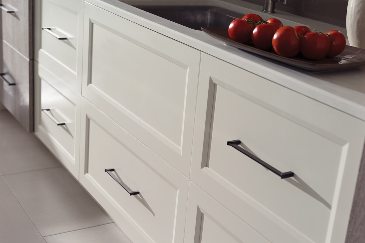 A row of white painted flat panel drawer fronts in a transitional kitchen design. When considering cabinet construction methods, cabinetry is divided into two major categories — Framed and Frameless. What’s the difference between Framed and Frameless kitchen cabinetry? This modern kitchen shows full overlay cabinet doors on frameless construction.