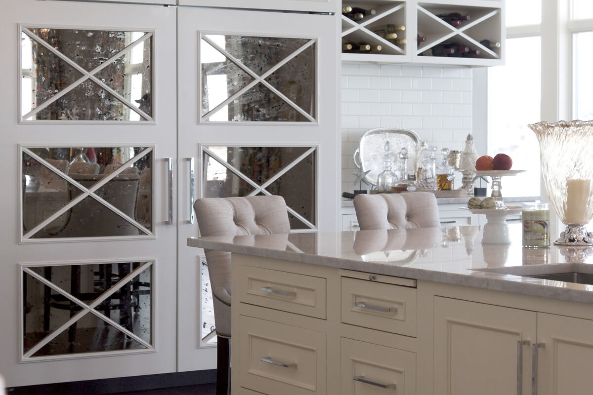 A cabinet paneled French door refrigerator with mirrored mullion insets to hide the large kitchen appliance.