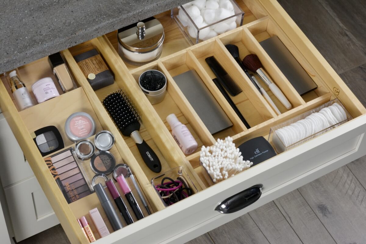 An organized bathroom drawer with dividers and tiered tray for cosmetics and beauty supplies.