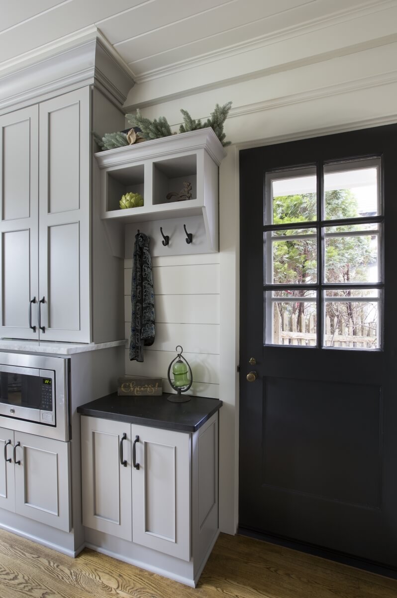 A light gray entryway cabinet with coat hooks at the entry way of the kitchen with white shiplap walls.