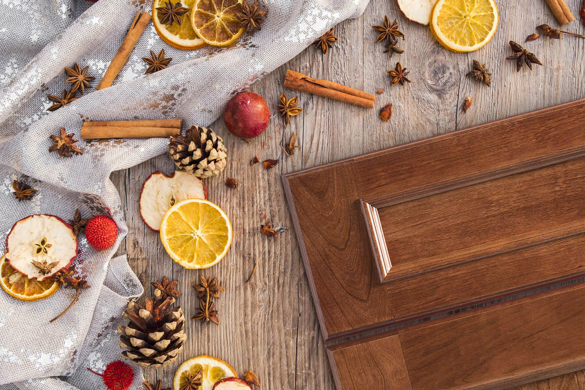 A flat panel cabinet door style with a delicious, red-orange stained finish on cherry wood. Cinnamon sticks and cider supplies are scattered around the door on a table to emphasize the warm stain color.