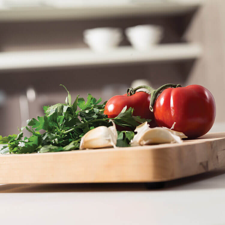 A close up of a cutting board with veggies on a countertop in a new kitchen.