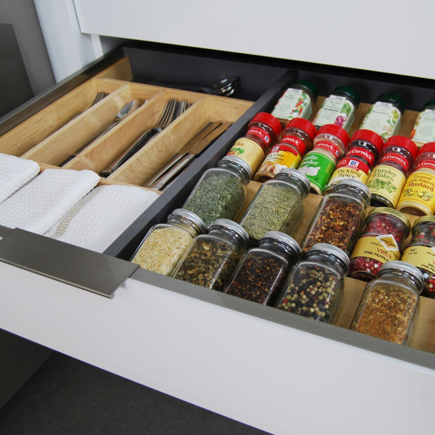 A stainless steel cabinet drawer with a metal partition and a wooden spice rack and wooden silverware utensil organizer.