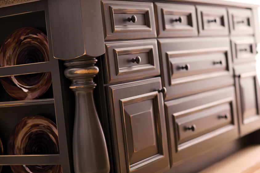 A close look at the cabinet doors and drawers on a rustic styled kitchen island that has an applied molding detail and distressed rub-thru paint finish.