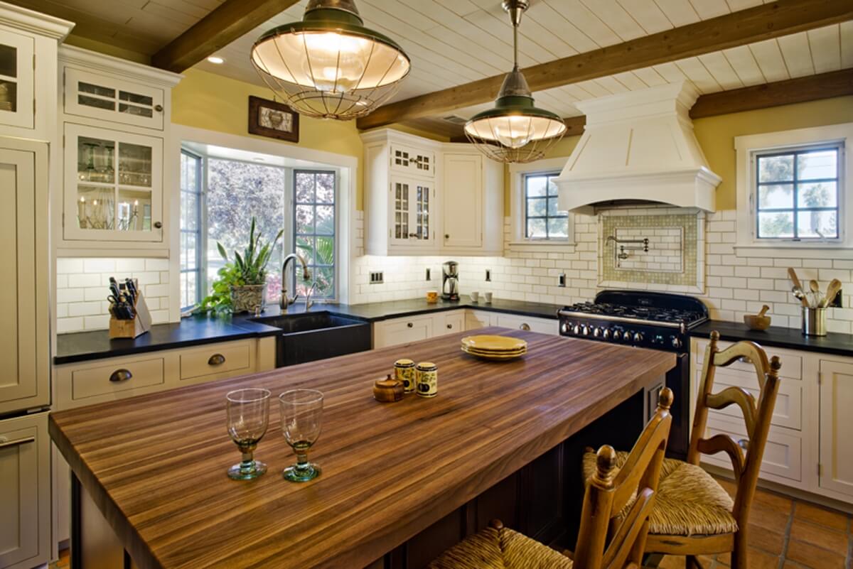 Dura Supreme Cabinetry kitchen design by Linda Williams of Hahka Kitchens. A classic farmhouse kitchen design with cottage styling features and old fashioned styled white oven, white cabinets, glass doors, a table styled kitchen island with a wood contertop and an apron sink with a window view.