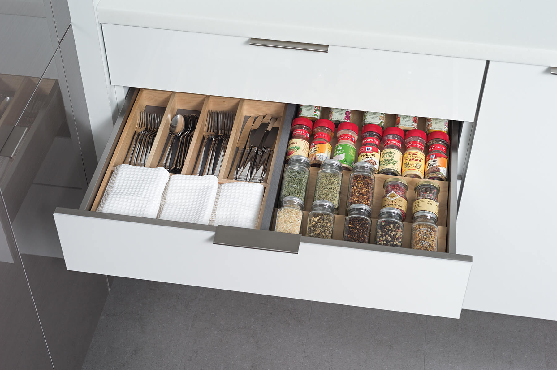 A stainless steel cabinet drawer with a metal partition and a wooden spice rack and wooden silverware utensil organizer.