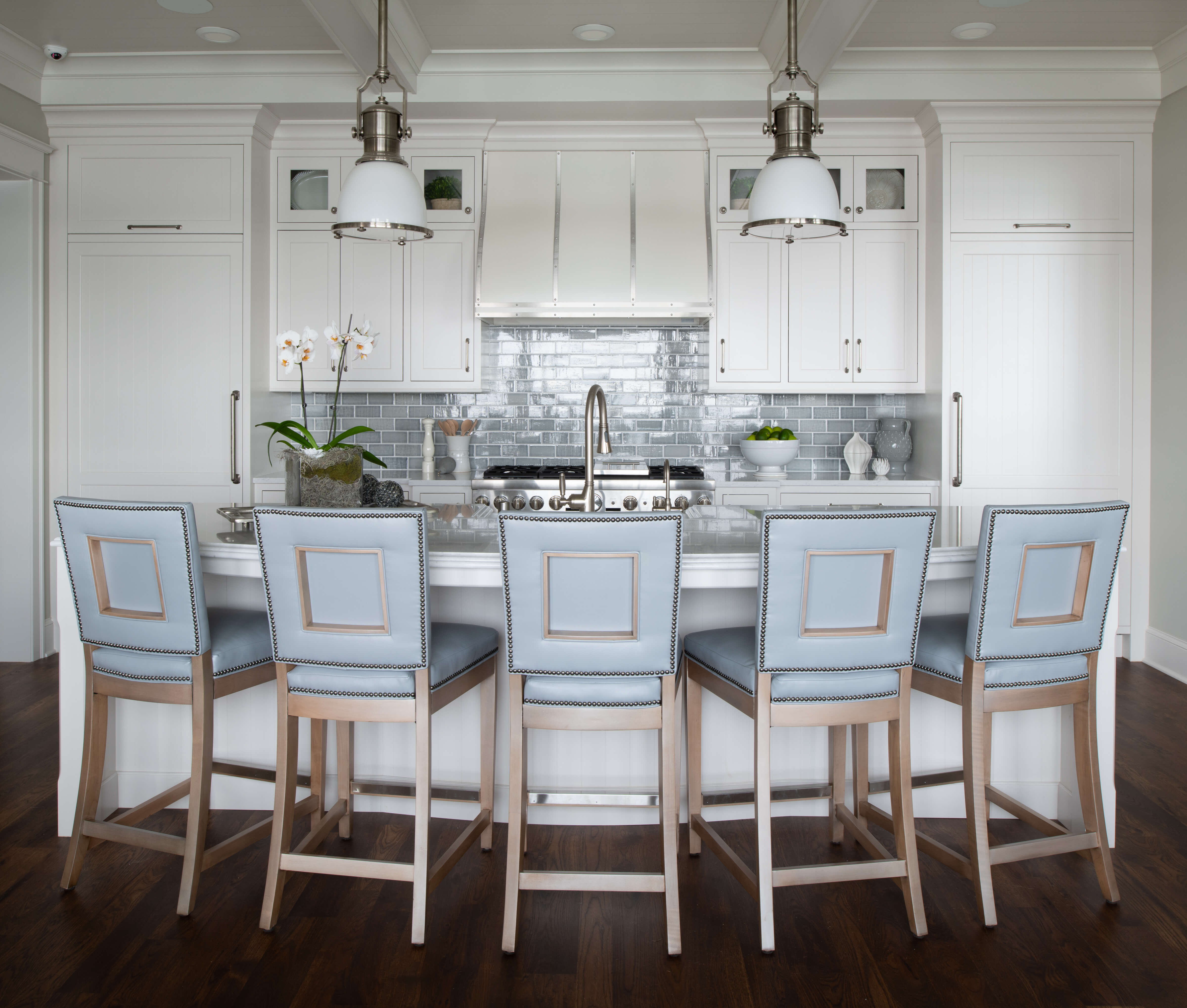 A symetrical kitchen design with an East Coast Shingle style using white inset cabinets, a light blue backsplash, pastel blue bar stools, and shiplap details.