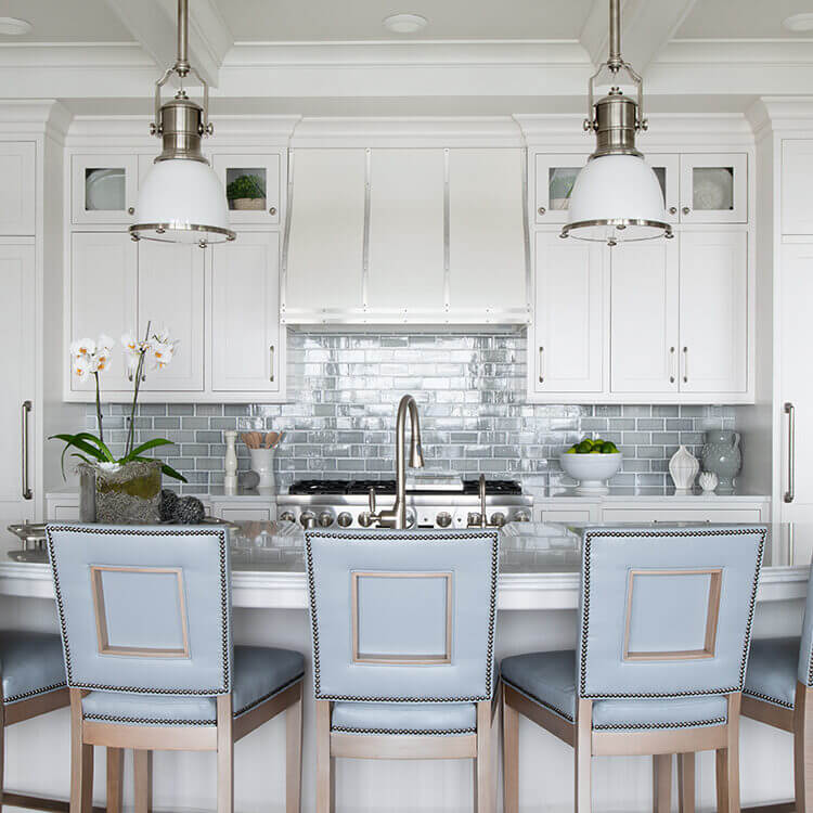 A symetrical kitchen design with an East Coast Shingle style using white inset cabinets, a light blue backsplash, pastel blue bar stools, and shiplap cabinet details.