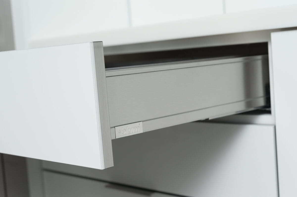 A close up of a stainless steel drawer with contemporary kitchen cabinets with an acrylic finish.