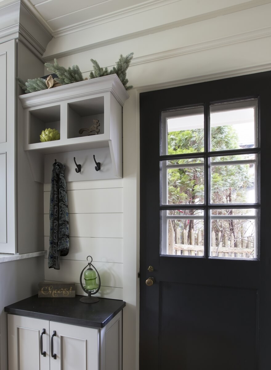 A light gray entryway cabinet with coat hooks at the entry way of the kitchen with white shiplap walls.