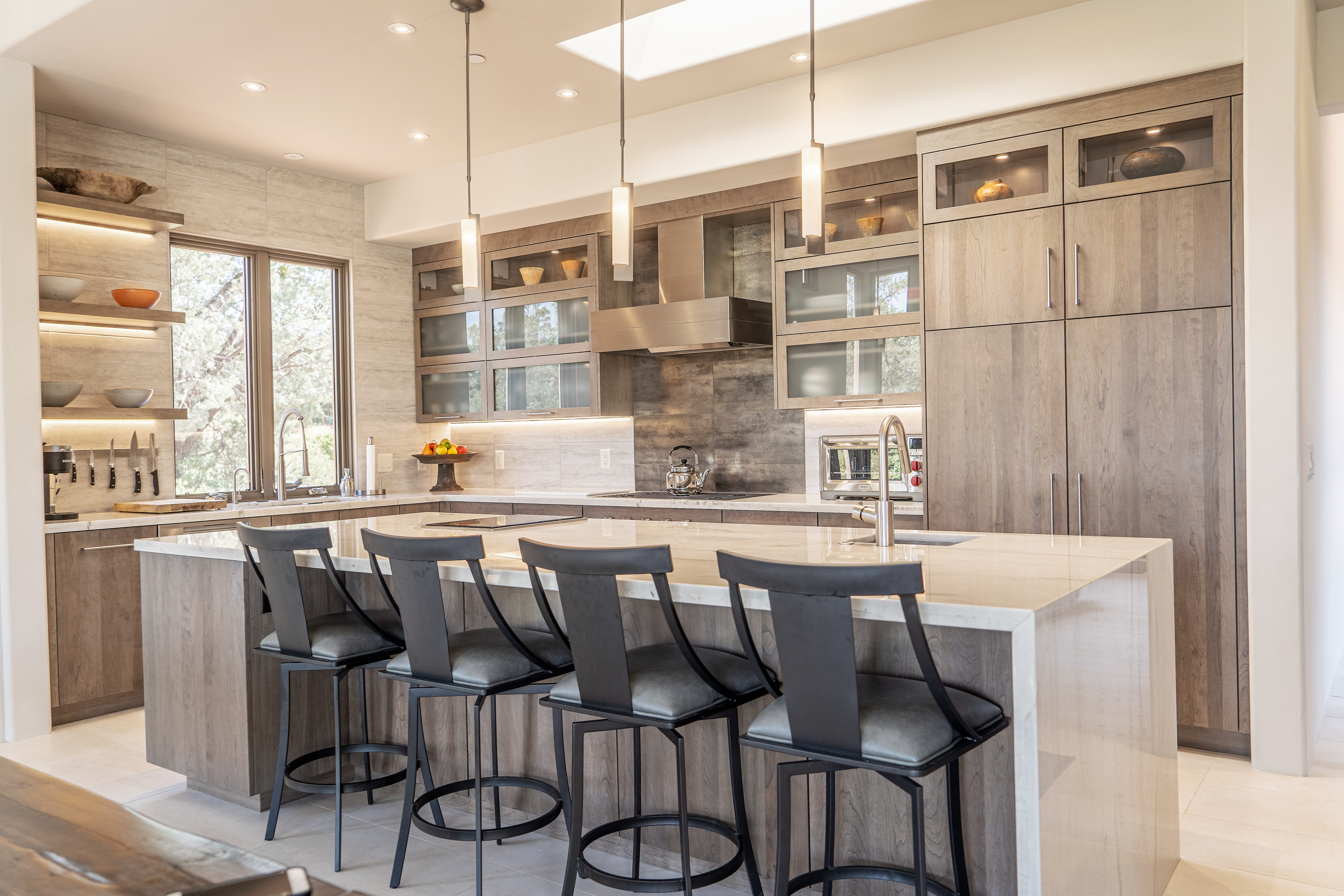 This modern kitchen has a waterfall kitchen island, seating for four, and stunning light gray-brown stained cabinets from Dura Supreme.
