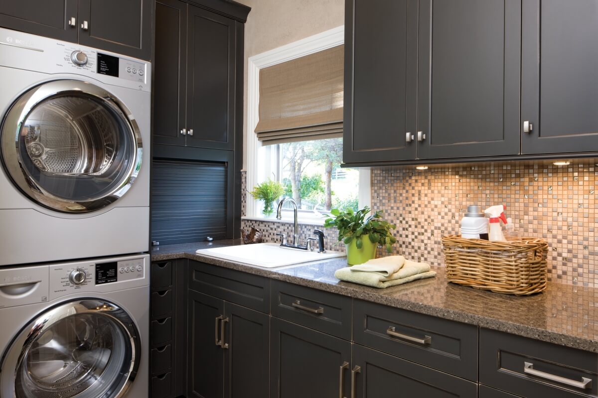 A laundry room remodel with almost black, dark gray painted cabinets from Dura Supreme Cabinetry with stainless steel appliances.