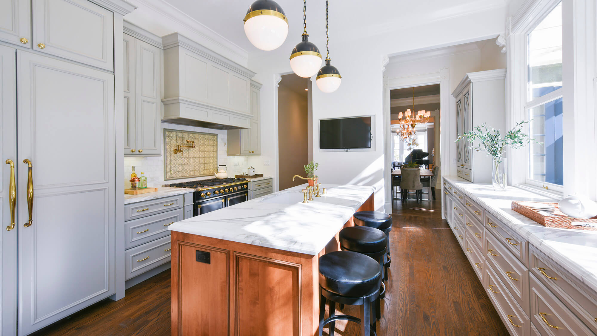 Beautiful slide-in range with double ovens in a gray kitchen design with gray painted kitchen cabinets and light gray backsplash tiles. Gold hardware, pot filler, and accents add warmth to the cool color palette. A detailed wood hood adds elegance to the design.