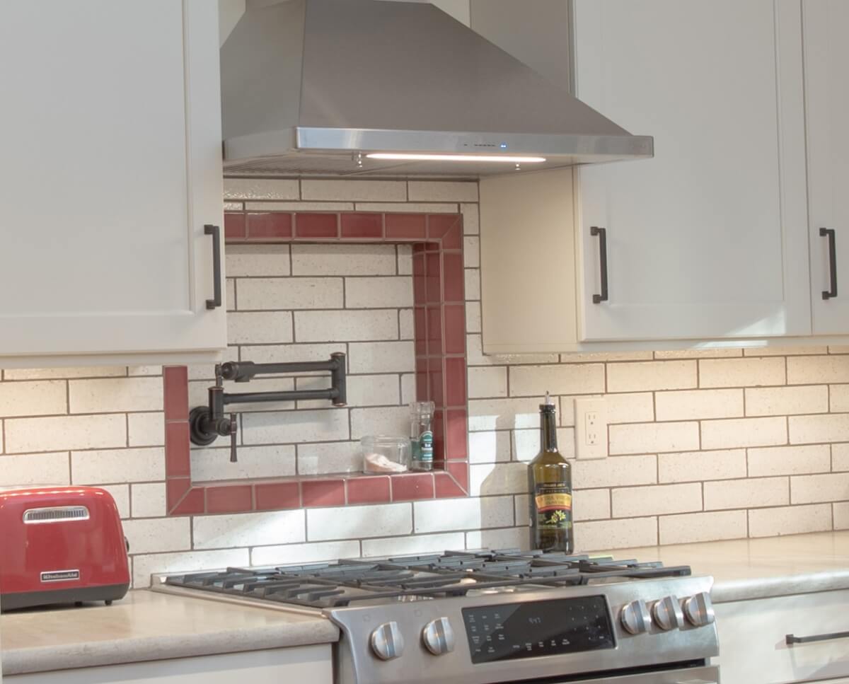 A close up of the cooking area with the tile framed pot filler above the cooktop.