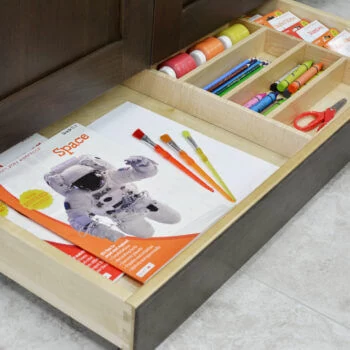 Miscellaneous items can find a home in a Dura Supreme Toe-Kick Drawer hidden at the foot of your cabinets. Add a Cutlery Divider for the extra organization to create a dedicated place for storing arts, crafts, and homework supplies. Place this solution near the dining room, a kitchen peninsula, or kitchen island where your household often sits to create a workstation that's easy to access and clean up.
