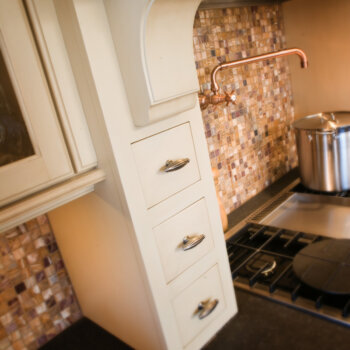 Wood hood storage from Dura Supreme using apothecary drawers in a tower that frame and add extra kitchen storage around the cooktop.