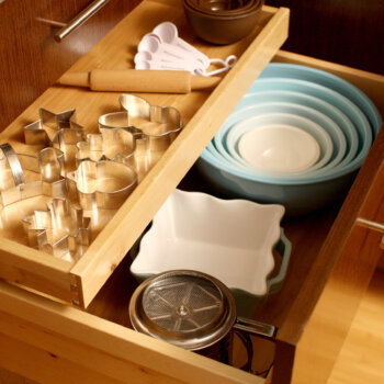 These baking supplies are stored in one spot by using a deep drawer for mixing bowls with a small roll-out tray for your cookie cutters and misc.items.