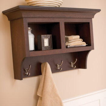 A wall organizer with coat hooks in a bathroom that coordinates with the bathroom cabinets.