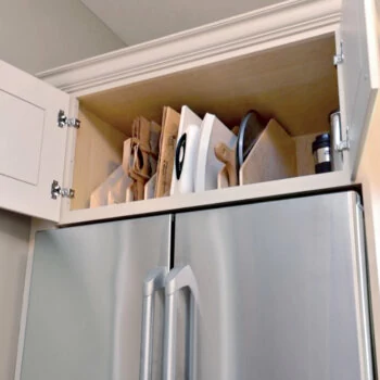 A cabinet tray divider kit in a wall cabinet above the fridge for sorting trays, pans, baking sheets, and cutting boards.