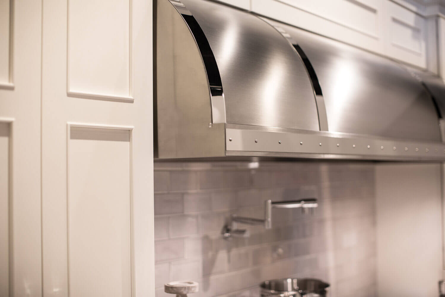 A close up of the stainless steel hood and white painted cabinets in a newly remodeled kitchen.