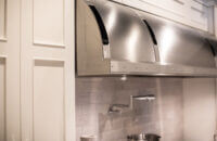 A close up of the stainless steel hood and white painted cabinets in a newly remodeled kitchen.