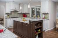 This classic two-tone kitchen remodel uses traditional overlay cabinet doors with raised panel styles. The 2-level kitchen island has a dark stained wood finish while the perimeter cabinets are painted bright white.