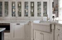 A traditional styled kitchen with white painted cabinets with a row of glass doors for dishware storage and display.