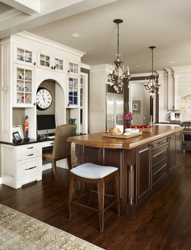 A traditional style kitchen with a built-in kitchen office desk with an arched detail and decorative glass cabinet storage.