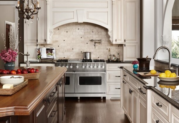A traditional white kitchen with a grand, elegant wood hood over a double-wide range.