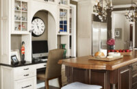 A traditional style kitchen with a built-in kitchen office desk with an arched detail and decorative glass cabinet storage.