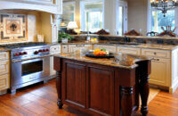 A stunning traditional styled kitchen design with a large wood hood and a table styled kitchen island.