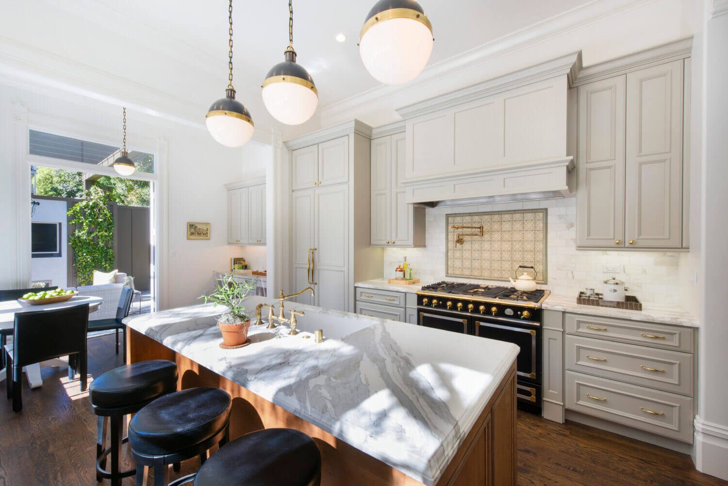 Beautiful slide-in range with double ovens in a gray kitchen design with gray painted kitchen cabinets and light gray backsplash tiles. Gold hardware, pot filler, and accents add warmth to the cool color palette. A detailed wood hood adds elegance to the design.