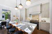 Beautiful slide-in range with double ovens in a gray kitchen design with gray painted kitchen cabinets and light gray backsplash tiles. Gold hardware, pot filler, and accents add warmth to the cool color palette. A detailed wood hood adds elegance to the design.