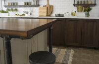 An industrial style kitchen remodel with modern and rustic cabinets. The distressed painted kitchen island has kitchen island stool stand made of pipe materials. Pipes are also used to accent the floating shelves below the wall cabinetry for displaying spices and hanging everyday cooking utensils.