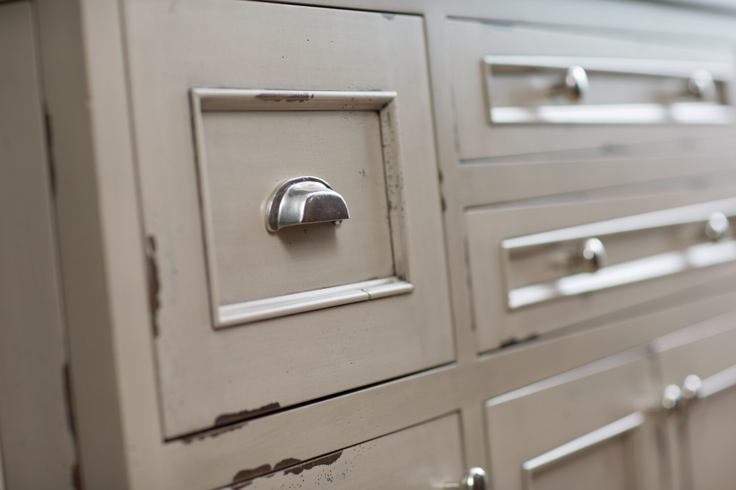 A close up of the distressed cabinets on a kitchen island with the Marley-Inset door style in a Heritage Paint “K” finish on Knotty Alder.