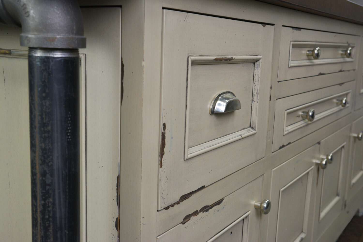 A close up of the distressed cabinets on an industrial style kitchen island with the Marley-Inset door style in a Heritage Paint “K” finish on rustic Knotty Alder wood.