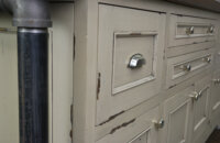 A close up of the distressed cabinets on an industrial style kitchen island with the Marley-Inset door style in a Heritage Paint “K” finish on rustic Knotty Alder wood.