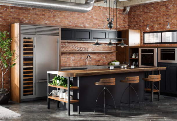 An Industrial style kitchen design in an urban loft with exposed brick walls and duct-work. The cabinets use a black painted finish and accents in a wood with a warm stain.