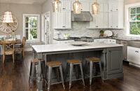 This transitional style kitchen was remodeled with white and rustic gray painted cabinets. The kitchen island features a distressed painted finish in a dark gray paint color with ornate turned posts and modern molding.