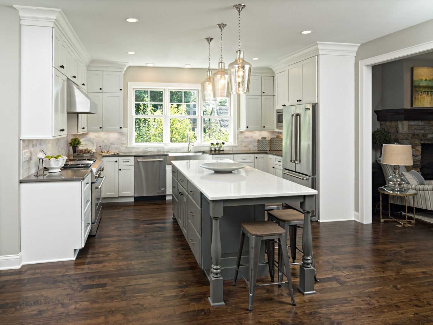 A remodeled kitchen with American-made cabinets. The kitchen island features a distressed painted finish in a dark gray paint color with ornate turned posts. The perimeter has white painted cabinets.