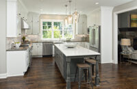 A remodeled kitchen with American-made cabinets. The kitchen island features a distressed painted finish in a dark gray paint color with ornate turned posts. The perimeter has white painted cabinets.