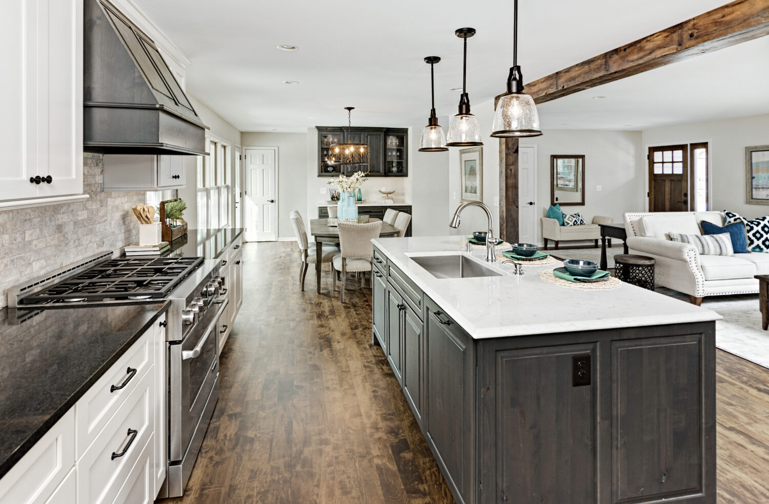 A view from the kitchen over the kitchen island into the dining room with white painted and gray stained cabinets and a classic style.