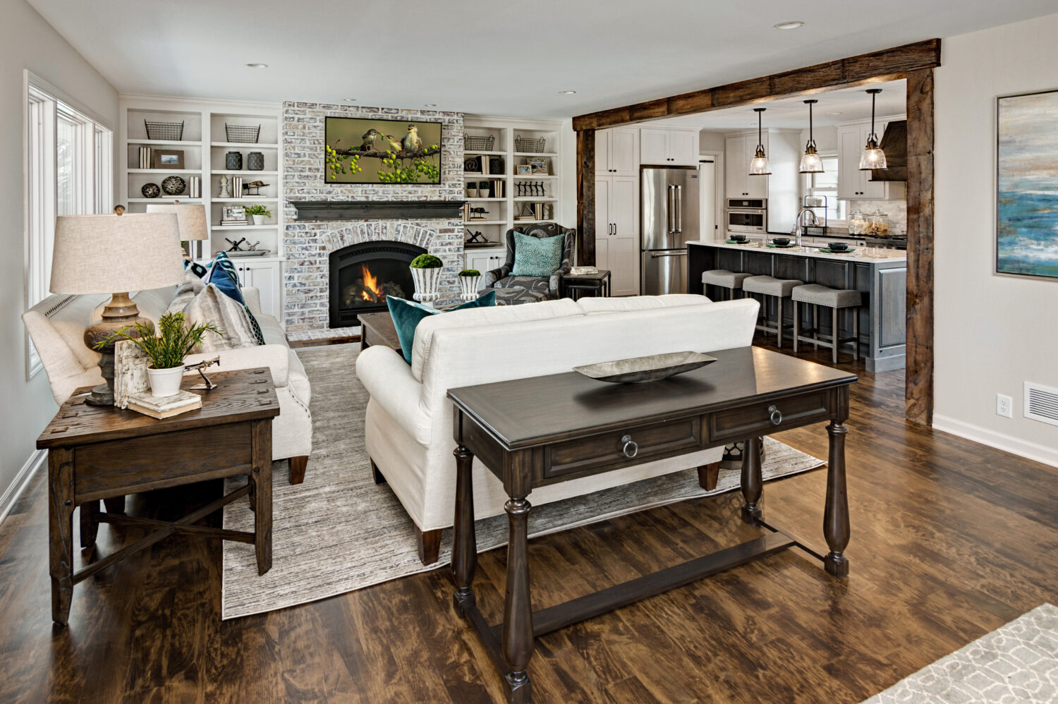 A beautiful living room next to the kitchen with a built-in entertainment center around the fireplace with white painted bookcases and cabinets and a dark gray stained fireplace mantel shelf.